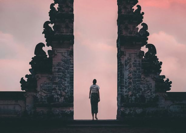 Serene sunrise view of a person standing at Lempuyang Temple's gateway, Bali, Indonesia.