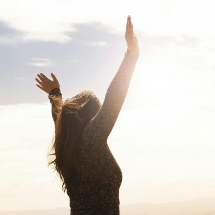 A woman with raised arms enjoying the bright open sky in a serene outdoor setting.